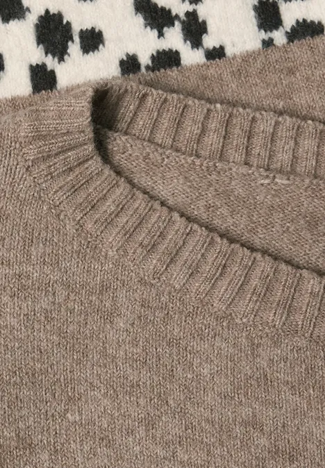 Sweter Jacquard z długim rękawem w stylistyce żakardowej z dekoltem w kształcie łódki sanded amber mel. Zbliżenie na jasnobrązowy sweter z okrągłym dekoltem, leżący na czarno-białej wzorzystej tkaninie.