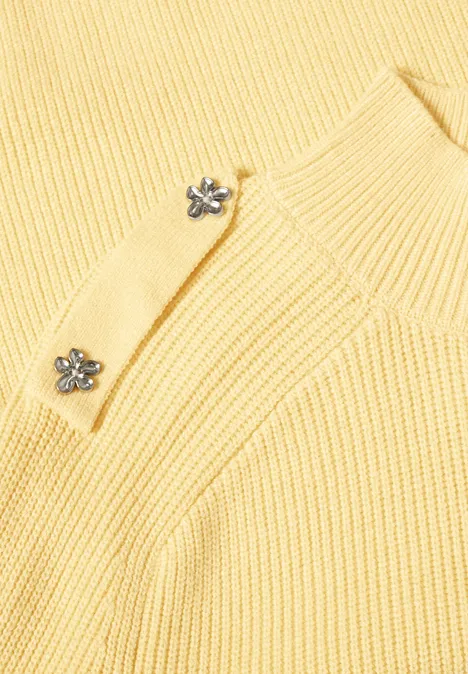 Gelber, gerippter Pullover mit eleganten silbernen Blumenknöpfen.