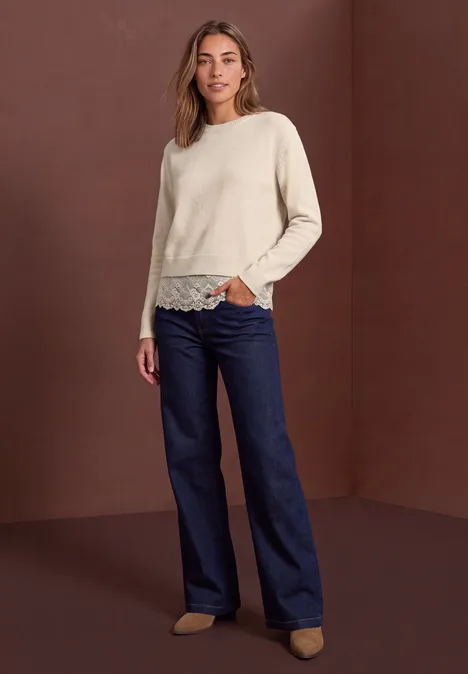 Ein Model trägt einen hellen Pullover mit Spitzenbesatz und weite dunkelblaue Jeans.