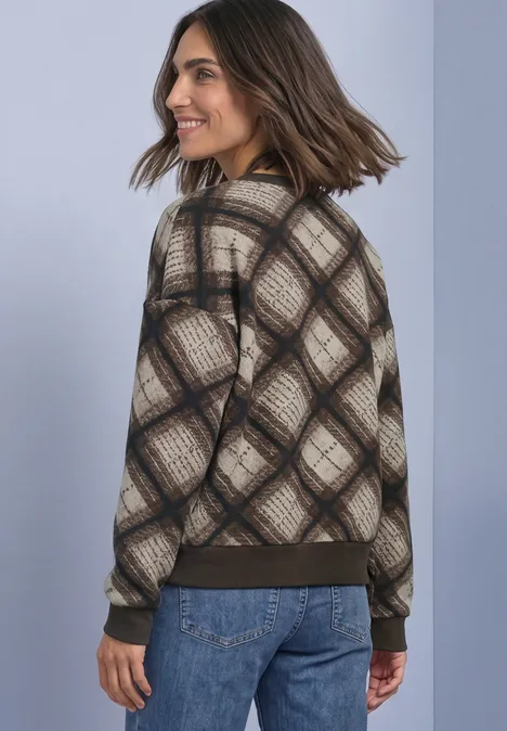 Frau im karierten Pullover und Jeans, lächelnd zur Seite blickend.