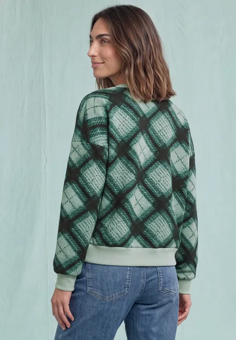 Frau von hinten in Jeans und grün kariertem Pullover vor hellem Hintergrund.