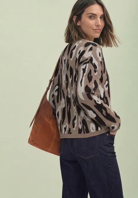 Vrouw met panterprinttrui, donkere jeans en bruine suède tas, kijkt over haar schouder.