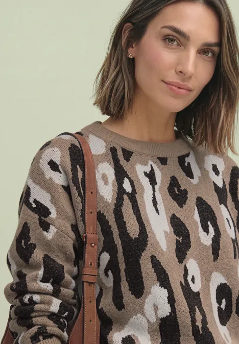 Vrouw met halflang bruin haar draagt een beige, bruine en zwarte luipaardtrui en een bruine schoudertas.