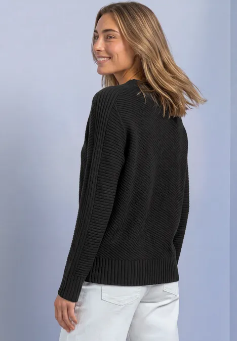 Frau in schwarzem Pullover und heller Hose blickt lächelnd über die Schulter.