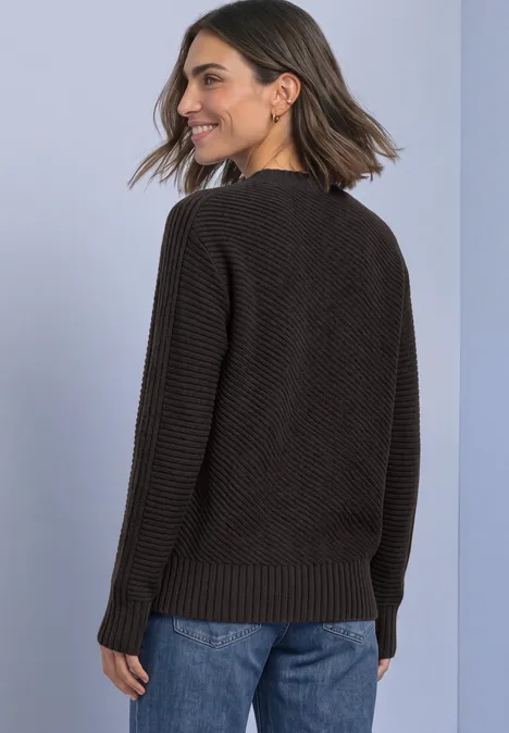Frau in schwarzem Strickpullover und blauen Jeans von hinten, mit schulterlangem Haar, lächelnd.