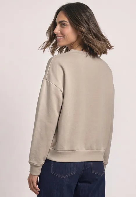 Loose Fit Sweatshirt mit Patch Detail clay sand Frau im beigen Sweatshirt mit langen Ärmeln und blauen Jeans, Rückansicht.