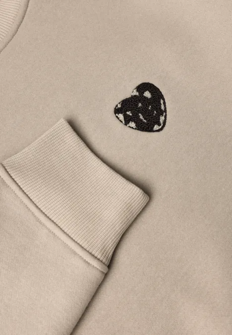 Loose Fit Sweatshirt mit Patch Detail clay sand Beiges Sweatshirt mit aufgesetzter Tasche und kleinem schwarzen Herzpatch mit weißen Dreiecksmustern.
