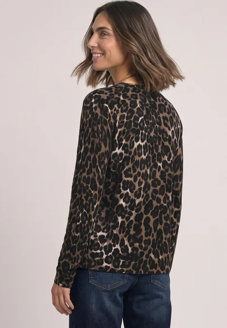 Eine Frau trägt einen braunen Leoparden-Pullover und blaue Jeans, schaut über die Schulter und lächelt.
