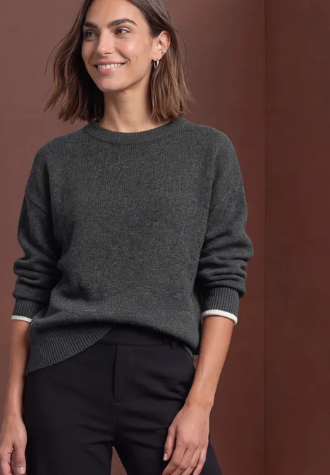 Pullover in Unifarbe mit Rundhals armor grey mel. Frau trägt dunkelgrauen Pullover und schwarze Hose, steht lächelnd vor braunem Hintergrund.