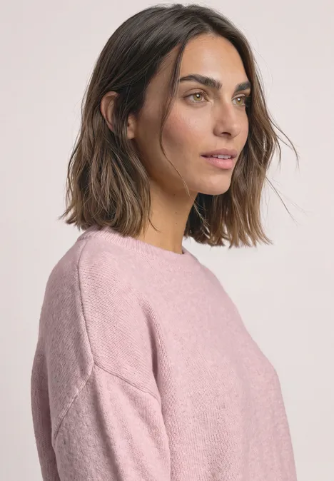 Porträt einer Frau mit braunen Haaren in rosa Pullover vor hellem Hintergrund, Blick seitlich rechts.