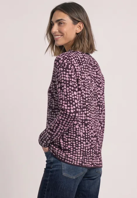Trui met col en jacquardpatroon berry plum Vrouw in zwart-roze printblouse en spijkerbroek, lacht en kijkt over haar schouder.