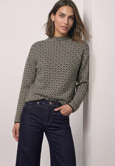 Pullover mit Turtle Neck und Jacquardmuster black coffee Eine Frau trägt eine gemusterte Langarmbluse und dunkle Jeans vor neutralem Hintergrund.