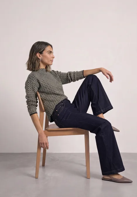 Pullover mit Turtle Neck und Jacquardmuster black coffee Eine Frau sitzt seitlich auf einem Stuhl, trägt grün-gemusterten Pullover, weite Jeans und flache Schuhe.