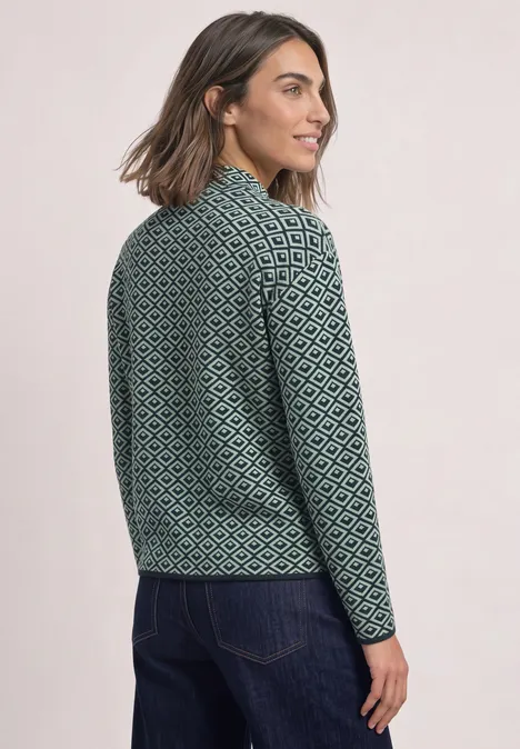 Pullover mit Turtle Neck und Jacquardmuster stormy green Frau steht seitlich im grünen, gemusterten Strickpullover und schaut über die Schulter.