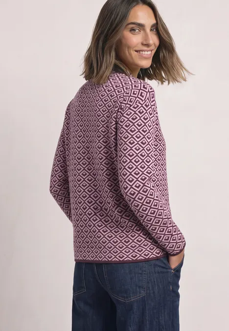 Pullover mit Turtle Neck und Jacquardmuster berry plum Eine Frau lächelt seitlich, trägt eine flieder-weiß gemusterte Strickjacke und blaue Jeans.