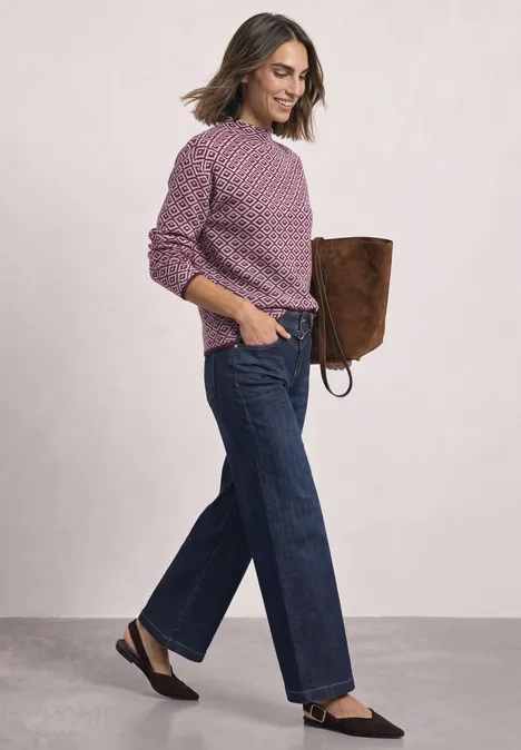 Pullover mit Turtle Neck und Jacquardmuster berry plum Frau in lila Strickpullover, weiten Jeans, schwarzen Slippern und brauner Tasche.
