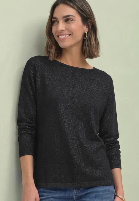 Dolman Pullover mit Glitzerdetails Black Eine lächelnde Frau trägt ein schwarzes, schimmerndes Langarmshirt vor hellem Hintergrund.