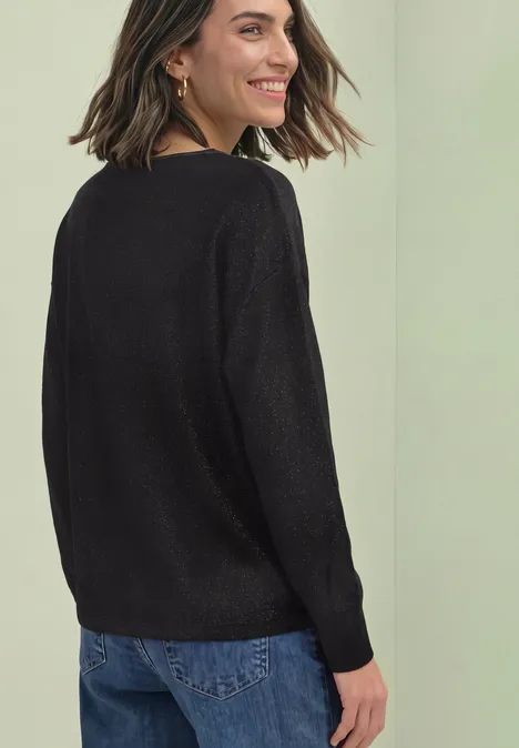 Dolman Pullover mit Glitzerdetails Black Frau trägt schwarzen Pullover, steht seitlich und lächelt leicht über die Schulter.