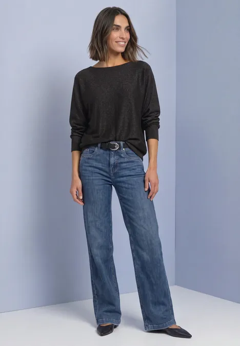 Dolman Pullover mit Glitzerdetails black coffee Frau in schwarzem Pulli und hoch taillierter, ausgestellter Jeans steht vor hellem Hintergrund, lächelnd.
