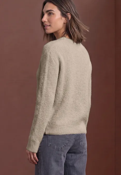 Trui van veergaren met V-hals clay sand Vrouw in beige fleecetrui en jeans kijkt over haar schouder voor een bruine achtergrond.
