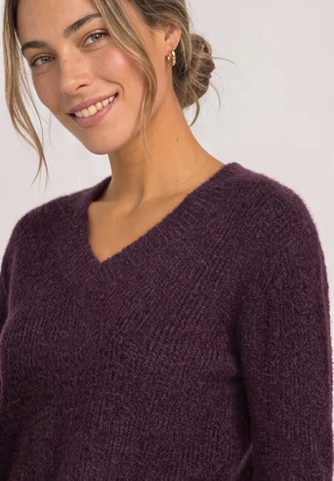 Trui van veergaren met V-hals berry plum Vrouw met blond knotje draagt violette gebreide trui met V-hals en lacht.