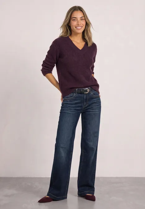 Trui van veergaren met V-hals berry plum Vrouw in donkere jeans en paarse trui voor een effen achtergrond.