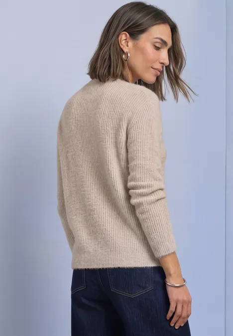 Federgarn Pullover mit Turtle Neck clay sand Eine Frau mit schulterlangen Haaren trägt einen beigen Pullover in leichter Rückansicht vor fliederfarbenem Hintergrund.