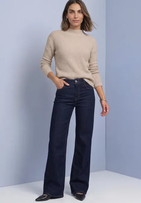 Federgarn Pullover mit Turtle Neck clay sand Frau in beigem Pullover und weitem, hoch tailliertem dunkelblauen Jeans vor hellem Hintergrund.