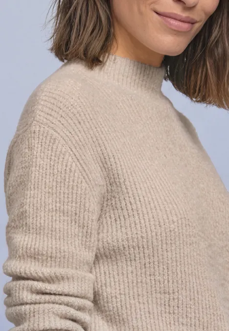 Federgarn Pullover mit Turtle Neck clay sand Frau mit schulterlangem braunem Haar trägt beigen, grob gestrickten Pullover, nur Oberkörper und leichtes Lächeln sichtbar.