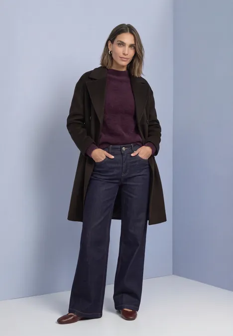 Federgarn Pullover mit Turtle Neck berry plum Eine Frau steht vor pastellblauem Hintergrund in Mantel, Pullover und weiten Jeans.