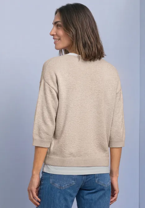 Pull à manches 3/4 et col en V clay sand mel. Frau von hinten in beigem Dreiviertelarm-Pullover und Jeans vor hellem, einfarbigem Hintergrund.
