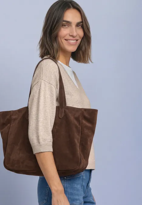 Pull à manches 3/4 et col en V clay sand mel. Junge Frau mit beigem Pullover und brauner Wildleder-Tasche vor hellem Hintergrund.