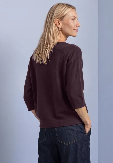 Pull à manches 3/4 et col en V berry plum Frau mit lockerem, dunkelviolettem 3/4-Ärmel-Pullover und Jeans, seitlich stehend, Hände in den Taschen.