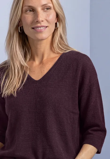 Pull à manches 3/4 et col en V berry plum Eine Frau mit blonden Haaren trägt einen dunkelvioletten V-Pullover mit 3/4-Ärmeln und Creolen.