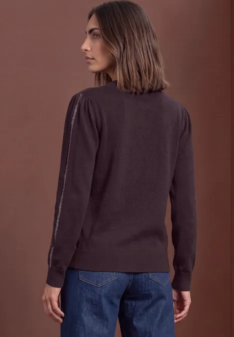 Une femme de dos portant un pull marron et un jean devant un fond uni.