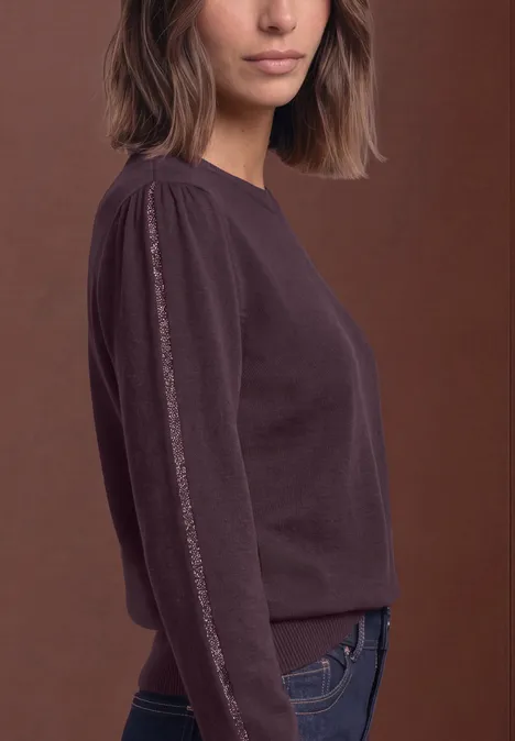 Portrait de profil d’une femme portant un pull bordeaux à manches longues sur fond marron.
