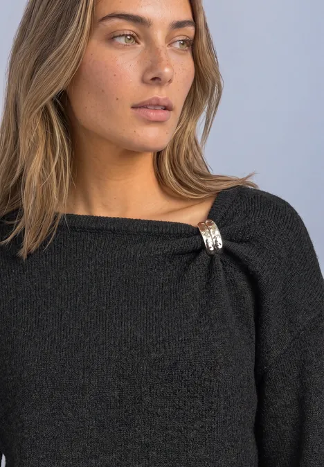 Femme aux cheveux clairs porte un pull noir pailleté avec un bijou scintillant au col.