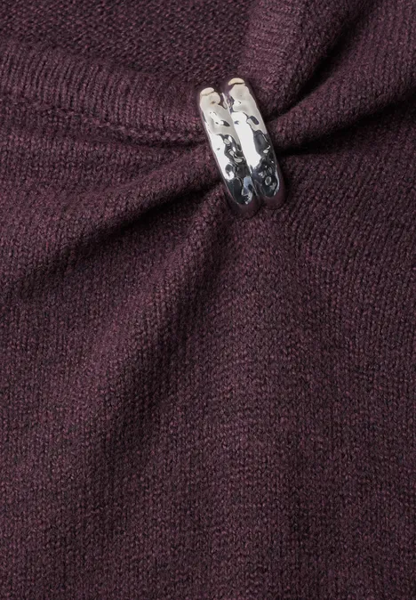 Pull à col bateau orné d'une broche berry plum mel. Nahaufnahme eines dunkelroten Strickpullovers mit silbernem Zierrahmen, der den Stoff zusammenhält.