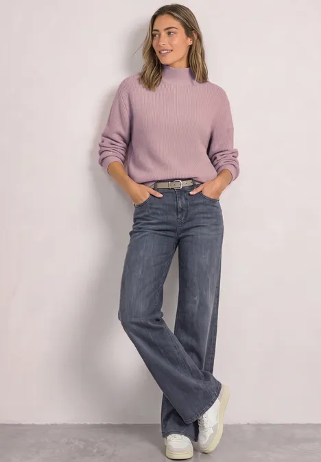 Pullover im Melange-Look mit Turtle Neck quiet rose mel. Frau in fliederfarbenem Pullover, weiten Jeans und weißen Sneakern vor schlichtem Hintergrund.