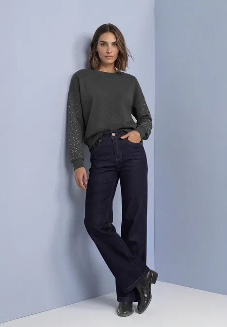 Loose Fit Sweatshirt mit Nieten armor grey mel. Modell mit dunkelgrünem Pullover, weiten Jeans und schwarzen Boots vor schlichtem hellblauem Hintergrund.