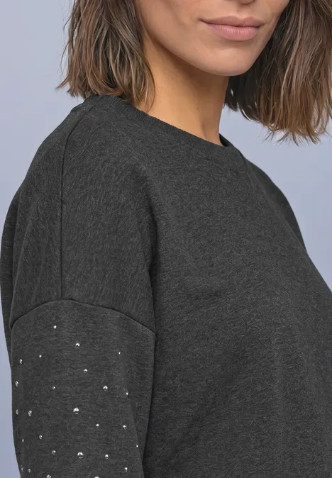Loose Fit Sweatshirt mit Nieten armor grey mel. Halbporträt einer Frau in dunkelgrauem Pullover mit kleinen Metallnieten am Ärmel.