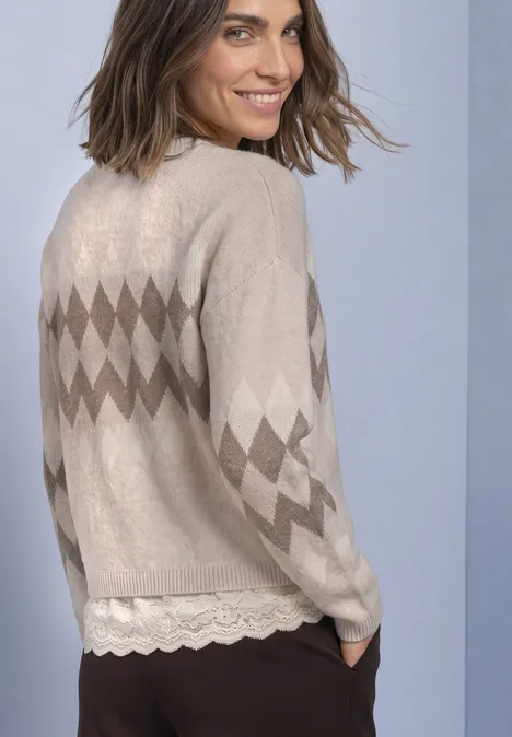 Pullover mit Jacquardmuster und Spitze clay sand mel. Dame in beiger Strickjacke mit Rautenmuster lächelt über die Schulter, darunter Spitzenbluse.