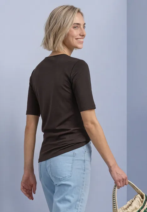 Vrouw in zwart T-shirt en lichtblauwe jeans, met een strooien tas, glimlachend over haar schouder kijkend.
