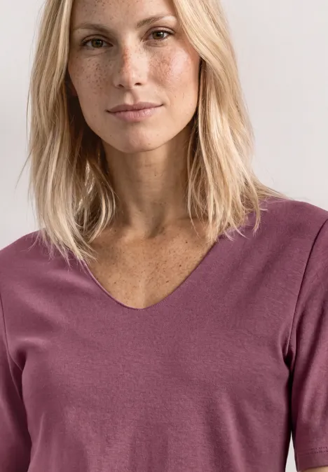 Porträt einer Frau mit langen blonden Haaren, Sommersprossen, dezentem Make-up und V-Ausschnitt-Pullover in Mauve.