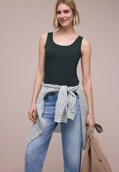 Frau mit schwarzem Tanktop, blauen Jeans, gestreiftem Pullover um die Taille und beiger Tasche.