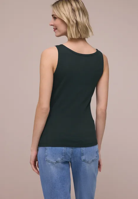 Rückansicht einer Frau in schwarzem Tanktop und blauen Jeans vor neutralem Hintergrund.