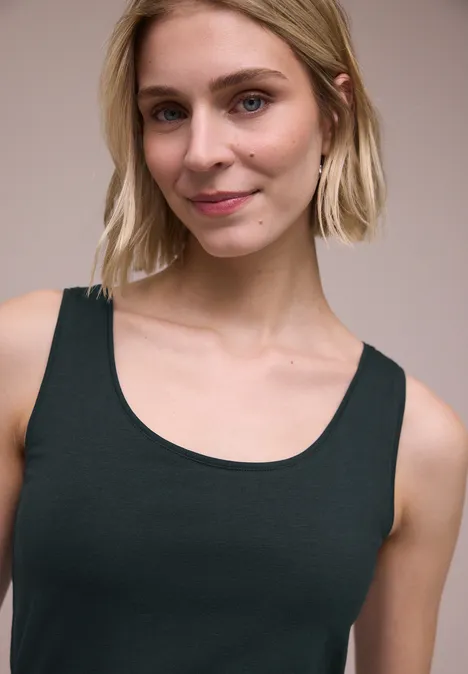 Oberkörper einer Frau in ärmellosem, schwarzem Top vor neutralem Hintergrund.