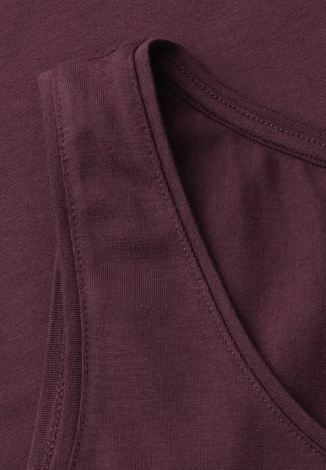 Close-up van een bordeauxkleurige mouwloze tanktop met zichtbare naden bij de halslijn.
