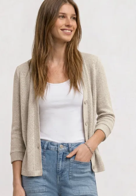Frau mit weißem Top, beiger Strickjacke und blauen Jeans.