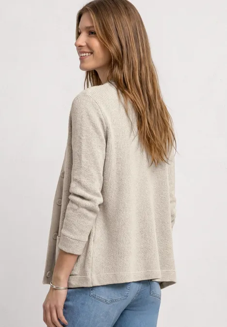 Frau von hinten in hellem Cardigan und Jeans vor neutralem Hintergrund.